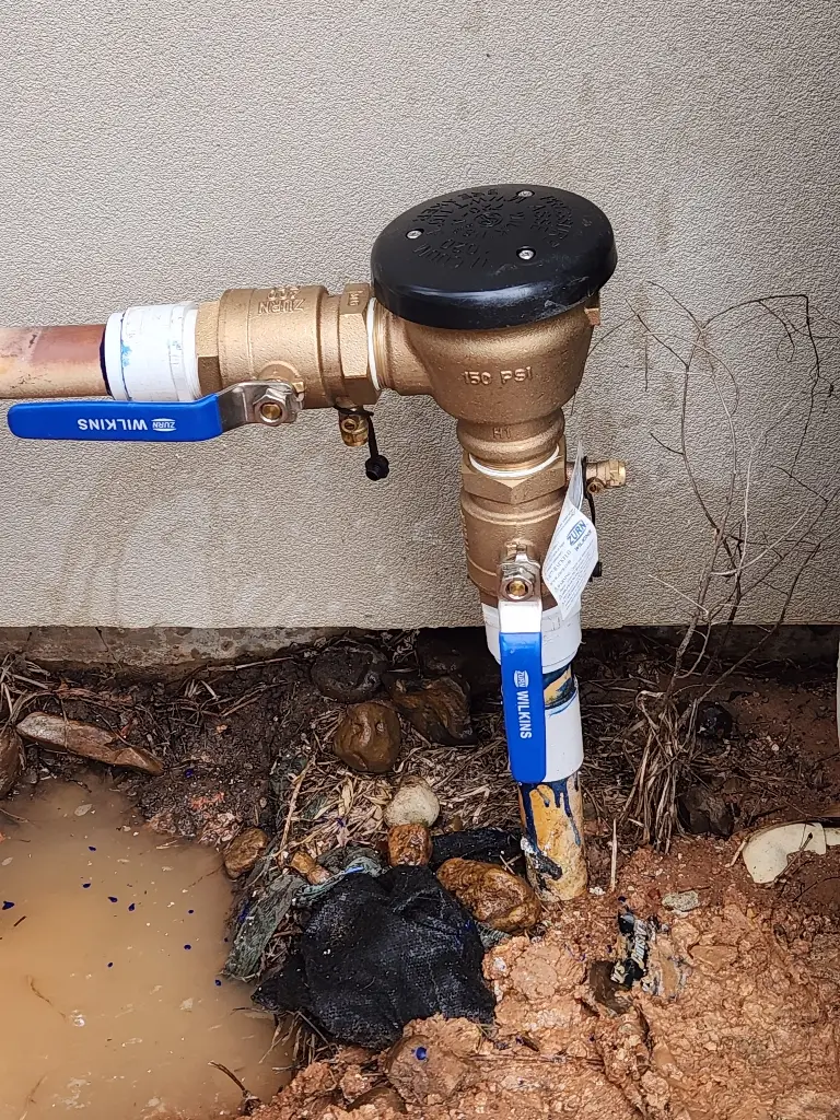 Brass irrigation backflow preventer assembly installed beside a house